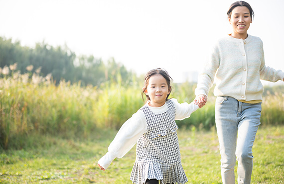 A little asian girl holding here mother's hand pulling her and running through a field