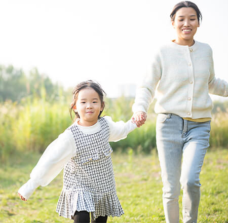 A little asian girl holding here mother's hand pulling her and running through a field