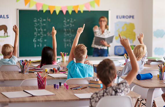 Elementary aged children raising their hands in a classroom
