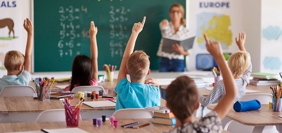 Elementary aged children raising their hands in a classroom