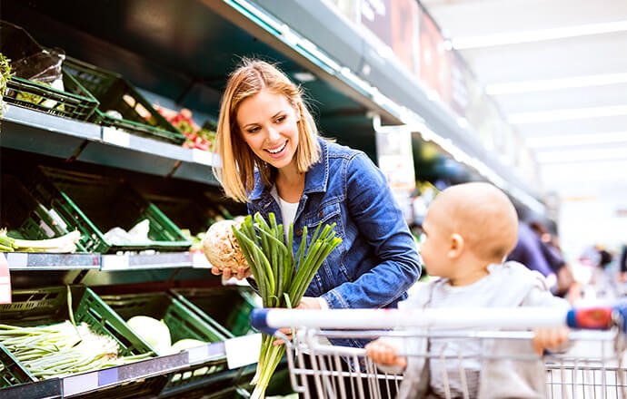 A woman grocery shopping with a baby in her shopping cart