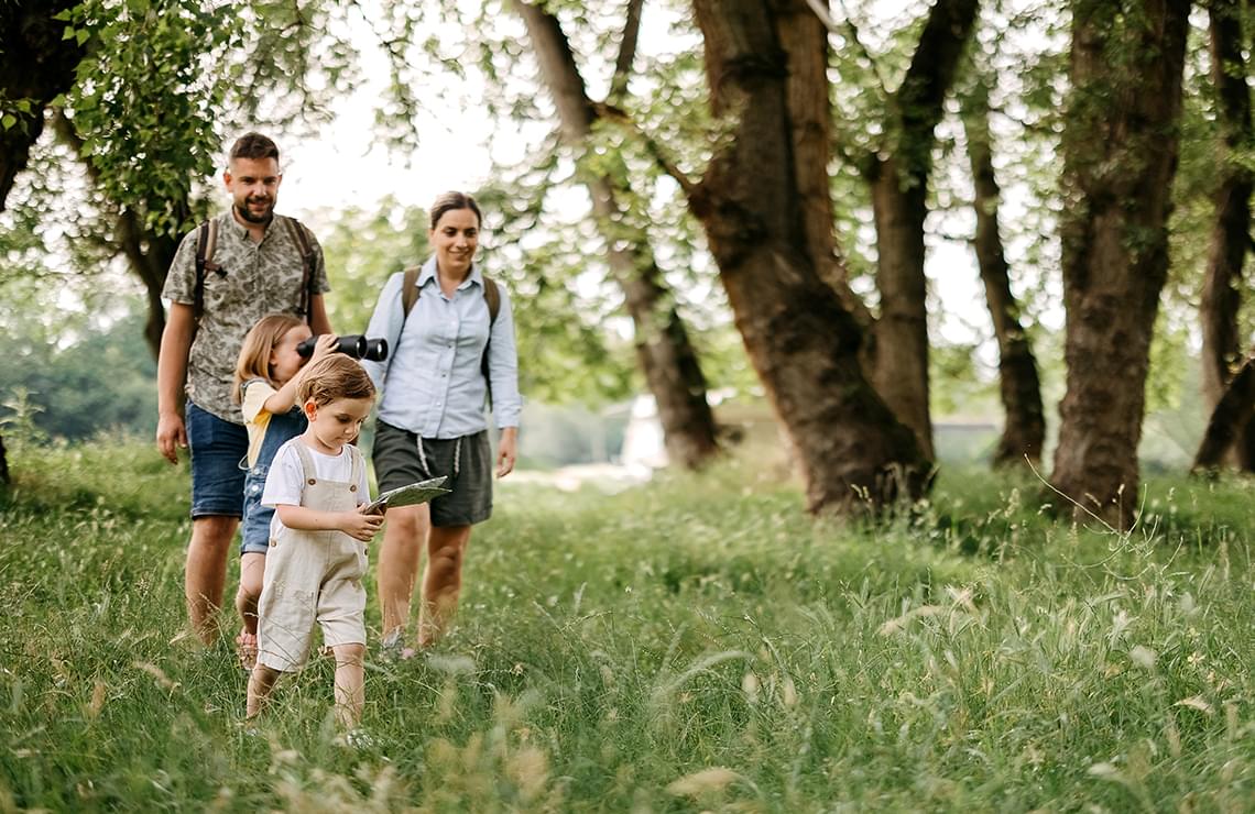 Family of 4 walking through a wooded/grassy area