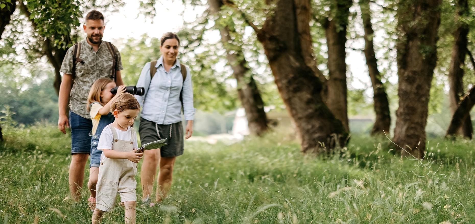 Family of 4 walking through a wooded/grassy area